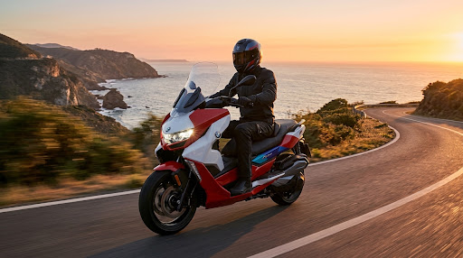 A rider on the scooter on a winding coastal road at sunset.